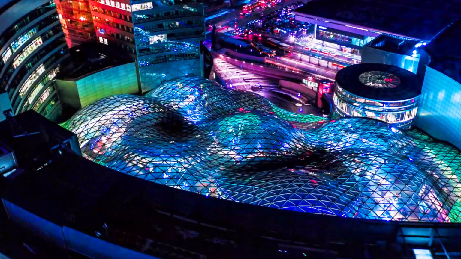 Warszawa w Barwach Tokyo. Widok na Złote Tarasy z góry, przeszklona konstrukcja zaokrąglonych kopuł podświetlona jest na niebiesko, wyraźnie widać trójkątną teksturę kopuł.