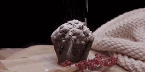 muffina centracalnie ułożona w kadrze na czarnym tle stoi na bambusowej desce obok gałązki wrzosu w tle różowy kocyk
