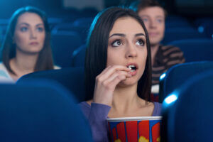 Kobieta w kinie. Atrakcyjna młoda kobieta jedząca popcorn i oglądająca film siedząc w kinie, podziwia scenę o darmowym zapytaniu o wycenę na film promocyjny. Aktualności