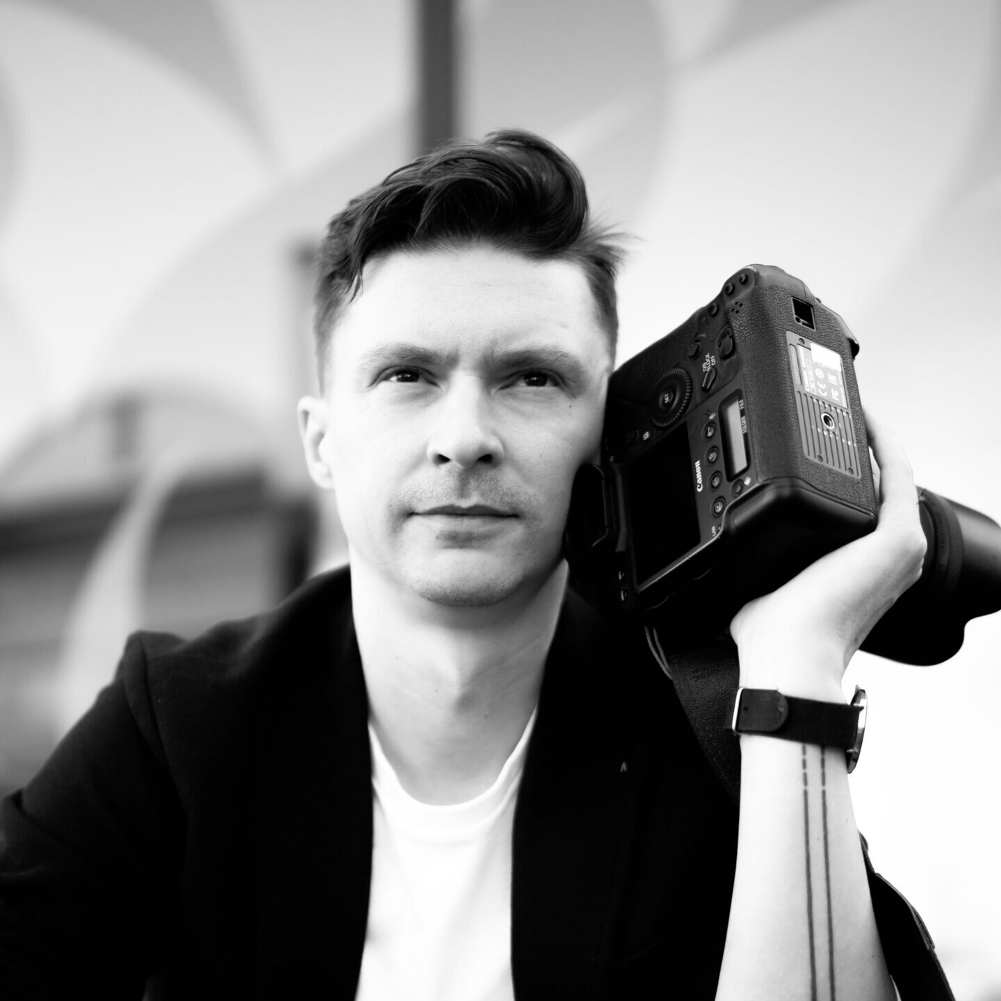 Dariusz Goldmann trzyma profesjonalny aparat fotograficzny, wykonując autoportret. Skupiona sylwetka i sprzęt są głównym elementem kadru.