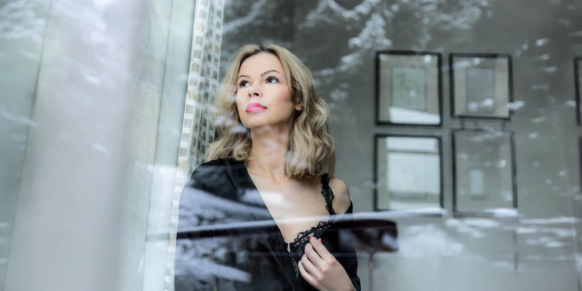 Portret kobiety stojącej przy oknie, z subtelnymi odbiciami w szybie.